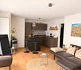 Modern living room and kitchen area with a dark brown sofa, round coffee table, bar stools, and a kitchen island with bar stools. Features a large mirror, artwork, and decorative items.