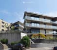 Modern multi-story residential building with balconies, glass railings, and a raised ground floor entrance.