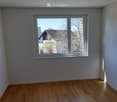 Empty room with wooden flooring and large window showing outdoor view.