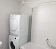 Bathroom with a bathtub, a washing machine, and a dryer stacked vertically.