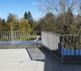 Modern balcony with grey tiled floor, metal railing, and a view of trees and a clear blue sky.