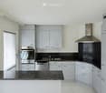 Modern kitchen with grey cabinets, stainless steel appliances, black countertops, and a large window with blinds.