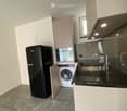 Modern kitchen with white cabinets, black countertop, stainless steel sink, and appliances including a refrigerator and washing machine.