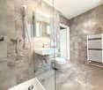 Modern bathroom with marble tiles, glass shower enclosure, white sink, toilet, and a built-in radiator.