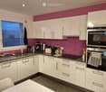 Modern kitchen with white cabinets, granite countertop, stainless steel appliances, and a pink accent wall.