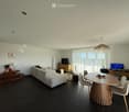 Modern living and dining area with a grey sectional sofa, round wooden dining table, chairs, a TV, and decorative items on a side table.
