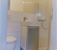 Modern bathroom with white tiles, a toilet, a sink with a faucet, and a glass-enclosed shower area.