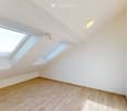Empty attic room with wooden flooring, white walls, and skylight windows allowing natural light to enter.