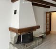 Room with exposed wooden beams, a stone fireplace with a wooden mantel, and a wooden floor.