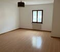 Empty room with wooden flooring, white walls, a single window with white curtains, a radiator, and a hanging pendant light fixture.