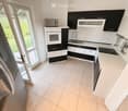Modern kitchen with black and white cabinets, stainless steel appliances, and a large window leading to a garden.