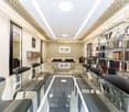 Modern office or meeting room with glass table, black chairs, bookshelf filled with books, large mirror, and decorative wall art.