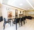 Modern living room with a glass dining table, black chairs, a sofa, a cabinet, and decorative wall art.