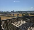 Balcony with wooden table and chairs, overlooking a rural landscape with fields and distant buildings.
