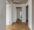 Modern hallway with wooden flooring, white walls, and a private washing machine in an adjacent room.
