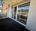Balcony with large glass sliding doors, black carpeted floor, and a view of surrounding buildings and greenery.