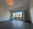 Empty room with wooden flooring, white walls, large sliding glass doors leading to a balcony, and a radiator on the wall.