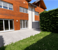 Modern two-story house with wooden siding, large windows, and a spacious patio area.