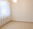 Empty room with beige tiled floor, white walls, large window with white curtains, and a modern pendant light fixture.