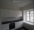 Modern kitchen with white cabinets, black countertops, and a decorative black and white tile floor. Features a sink, oven, and ample natural light from a large window.