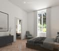 Modern bedroom with a large bed, nightstand, armchair, side table, cabinet, and decorative items. Large windows with sheer curtains and a view of greenery.