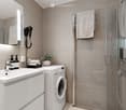 Modern bathroom with a white sink, mirror, washing machine, glass shower enclosure, and neatly arranged towels.