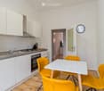 Modern kitchen with white cabinets, stainless steel appliances, and a small dining area with yellow chairs and a white table.