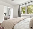 Cozy bedroom with a large bed, a mirrored wardrobe, and a window with curtains overlooking greenery.