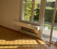 Empty room with wooden flooring, large window, and radiator below it. No furniture or equipment present.