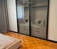 Modern bedroom with wooden flooring, a large mirrored wardrobe, and a neatly made bed with pillows.