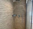 Modern shower area with wooden textured tiles, a glass partition, and a sleek showerhead and controls.
