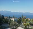 Panoramic view of a lake and mountains from a rooftop terrace, with surrounding buildings and greenery.