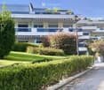 Modern multi-story residential building with balconies, surrounded by well-maintained greenery and a paved pathway.