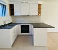 Modern kitchen with white cabinets, black countertops, a sink, and an oven. Features a window with a view and a wooden shelf on the right side.