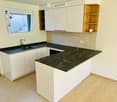 Modern kitchen with white cabinets, dark granite countertops, a sink, and a dishwasher. Features a wooden shelf and a window with a view.
