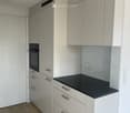 Modern kitchen with white cabinets, a black countertop, and a built-in oven. The floor is tiled in a warm, earthy tone.