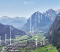 A panoramic view of a valley surrounded by mountains, with a town nestled in the valley floor and green fields interspersed with forested areas.