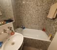 Bathroom with a white sink, bathtub, and mosaic tile walls. A mirror above the sink, and towels hanging on the side.
