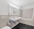 Modern bathroom with double sink, bathtub, shower, mirror, and decorative vase with flowers.