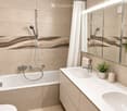 Modern bathroom with a bathtub, double sink vanity, large mirror, and a shower area with a glass enclosure. Features include a sleek faucet, a potted plant, and a soap dispenser on the counter.