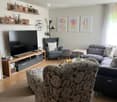 Modern living room with grey sectional sofa, armchair, coffee table, TV, shelves, and decorative items.