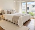 Modern bedroom with a large bed, multiple pillows, a blanket, and a table lamp on a wooden floor.