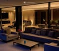 Modern living and dining area with a large sectional sofa, coffee table, dining table with chairs, fireplace, and a kitchen island with bar stools and potted plants.