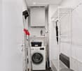 Compact utility room with a washing machine, ironing board, umbrella, ladder, and storage unit.