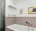 Modern bathroom with a bathtub, glass-enclosed shower, towel rack, and two framed pictures on the wall.