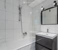 Modern bathroom with white tiled walls, a bathtub, a glass-enclosed shower, a sink with a modern faucet, and a large mirror with built-in lighting.