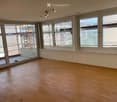 Empty room with wooden flooring, large windows, and track lighting. No furniture or equipment present.