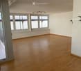 Empty room with wooden flooring, large windows, and modern lighting fixtures.