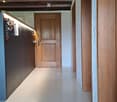 A long, narrow hallway with wooden doors and a polished white floor, featuring exposed wooden beams on the ceiling and recessed lighting.
