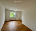 Empty room with wooden flooring, white walls, and a single window with white frame and blinds.